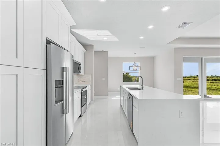 Kitchen with appliances with stainless steel finishes, recessed lighting, light countertops, white cabinetry, and a kitchen island with sink