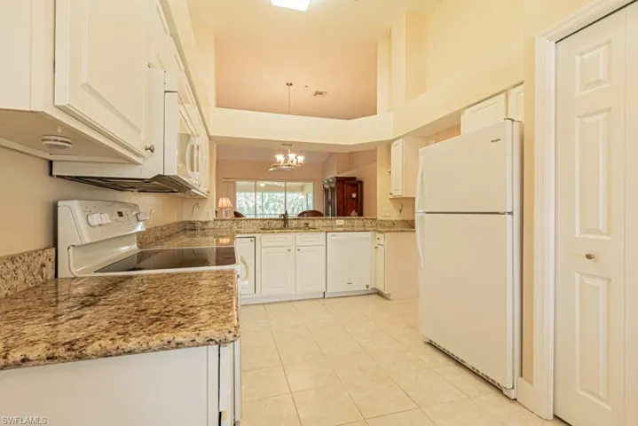 Kitchen with hanging light fixtures, white appliances, kitchen peninsula, white cabinets, and a towering ceiling