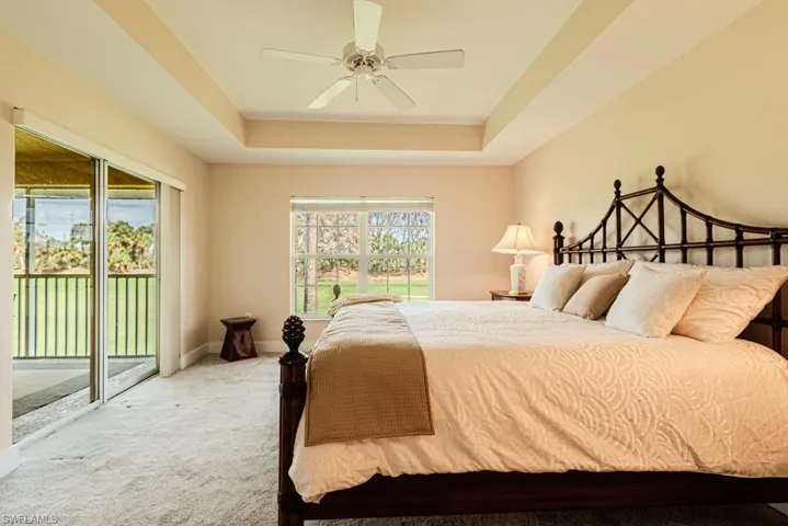 Carpeted bedroom featuring multiple windows, access to exterior, a tray ceiling, and ceiling fan