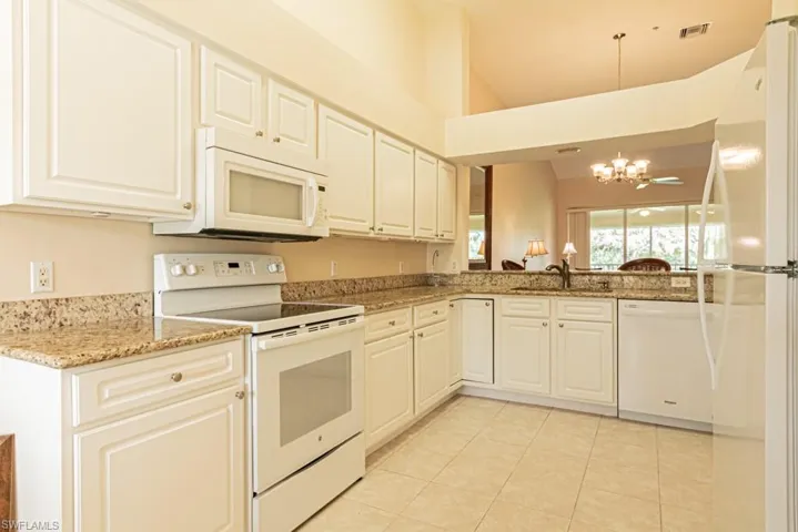 Kitchen featuring kitchen peninsula, white cabinets, a notable chandelier, sink, and white appliances