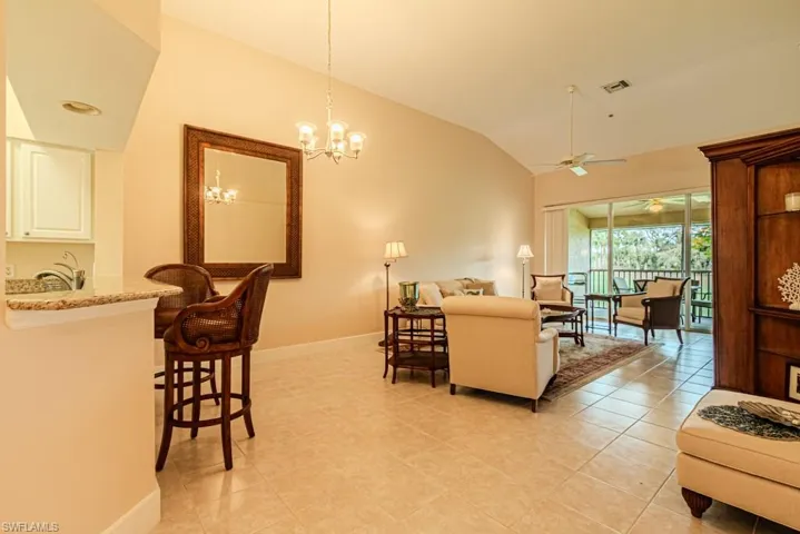 Living room with vaulted ceiling, ceiling fan with notable chandelier, and light tile patterned flooring