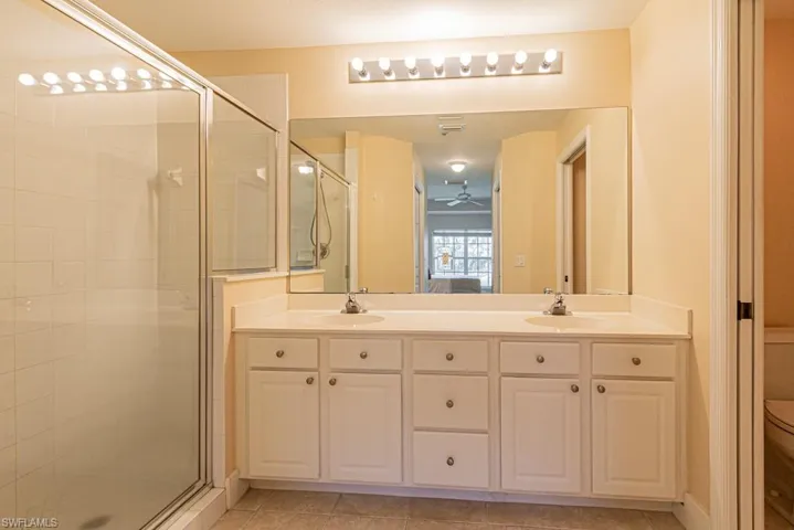 Bathroom featuring ceiling fan, toilet, a shower with shower door, vanity, and tile patterned floors