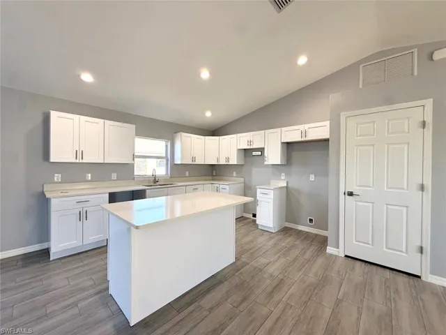 Kitchen with vaulted ceiling, white cabinetry, wood tiled floors, recessed lighting, and a kitchen island