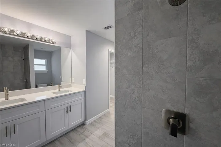 Full bath with tiled shower, double vanity, and wood tiled floors