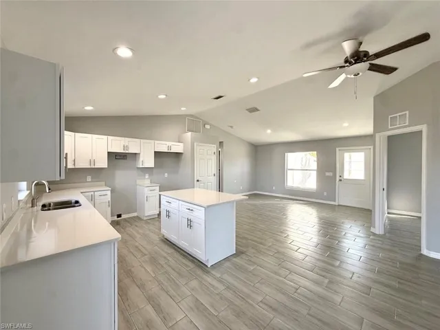 Kitchen featuring a center island, wood finish floors, vaulted ceiling, white cabinetry, and light stone counters