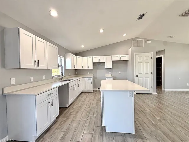 Kitchen with white cabinetry, wood finish floors, a center island, vaulted ceiling, and recessed lighting