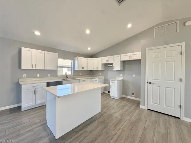 Kitchen featuring vaulted ceiling, white cabinetry, wood finish floors, recessed lighting, and a center island