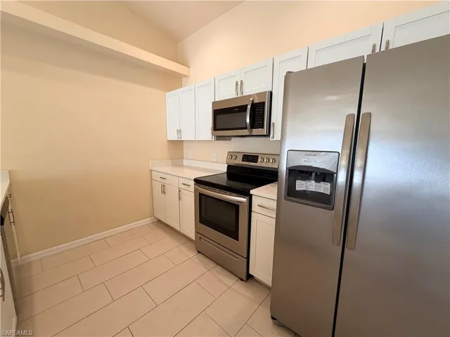 Kitchen with stainless steel appliances, white cabinets, and light tile patterned flooring