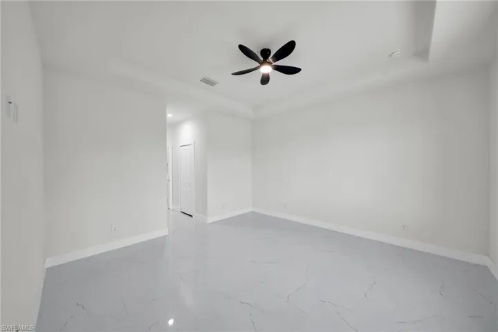 Empty room featuring a raised ceiling, ceiling fan, recessed lighting, and light marble finish floors