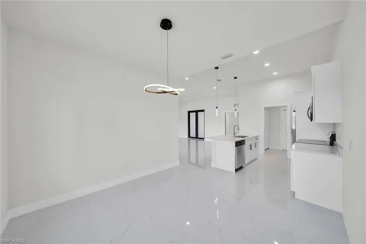 Kitchen featuring white cabinetry, open floor plan, light marble finish floors, stainless steel dishwasher, and a chandelier