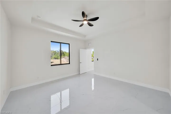 Unfurnished room with a tray ceiling, ceiling fan, and light marble finish floors
