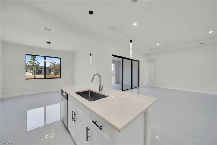 Kitchen featuring open floor plan, white cabinetry, decorative light fixtures, and light stone counters