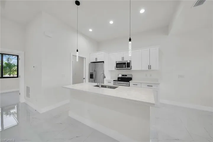 Kitchen with stainless steel appliances, light marble finish floors, white cabinetry, a kitchen island with sink, and hanging light fixtures