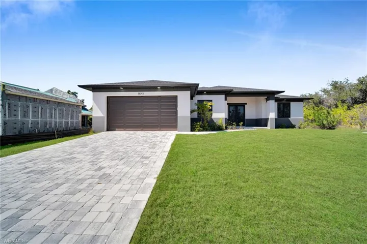 Prairie-style home featuring a front yard, stucco siding, decorative driveway, an attached garage, and french doors