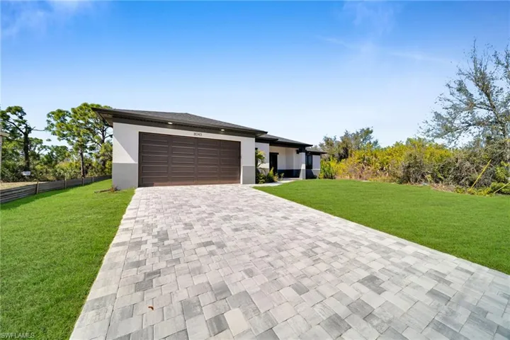 Prairie-style home featuring a front yard, decorative driveway, stucco siding, and an attached garage