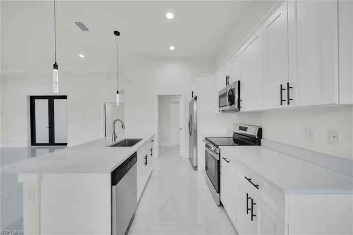 Kitchen with stainless steel appliances, white cabinetry, hanging light fixtures, an island with sink, and light marble finish flooring