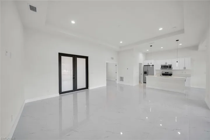 Unfurnished living room with french doors, a tray ceiling, recessed lighting, and light marble finish flooring