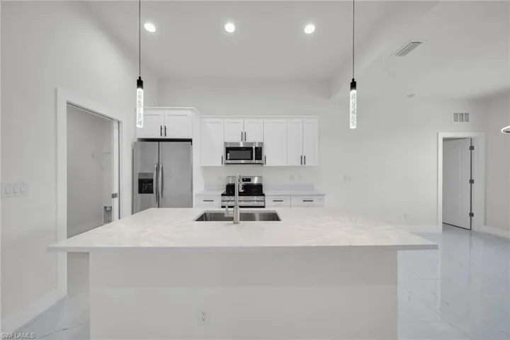 Kitchen with stainless steel appliances, white cabinetry, a kitchen island with sink, light stone countertops, and pendant lighting