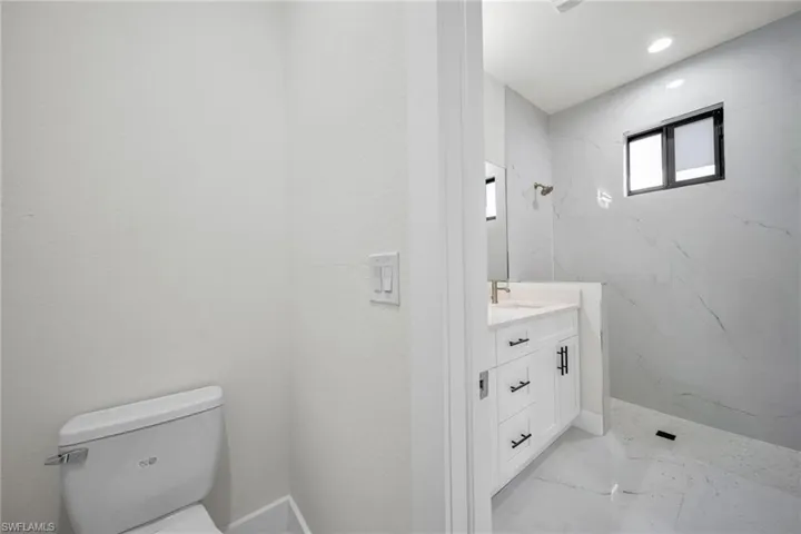 Bathroom featuring vanity, a marble finish shower, light marble finish floors, and recessed lighting