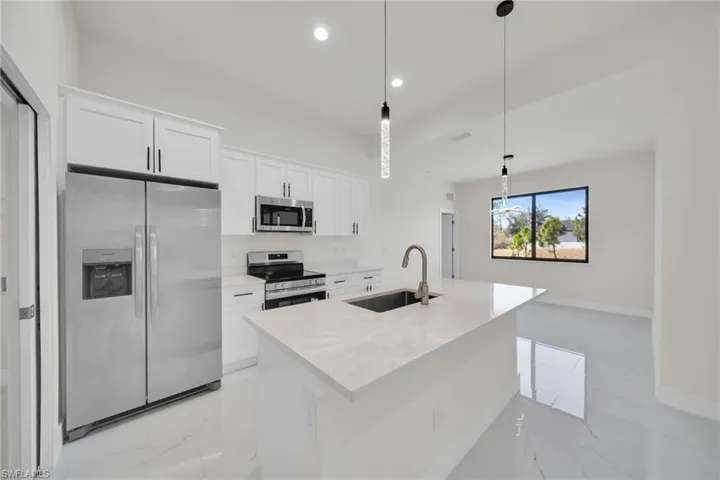 Kitchen featuring stainless steel appliances, white cabinetry, a center island with sink, light marble finish floors, and pendant lighting