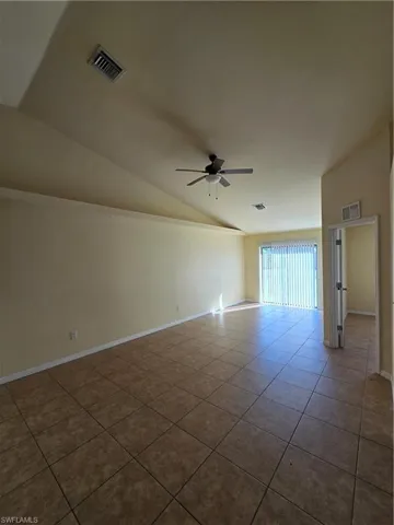 Empty room featuring vaulted ceiling, ceiling fan, and light tile patterned floors