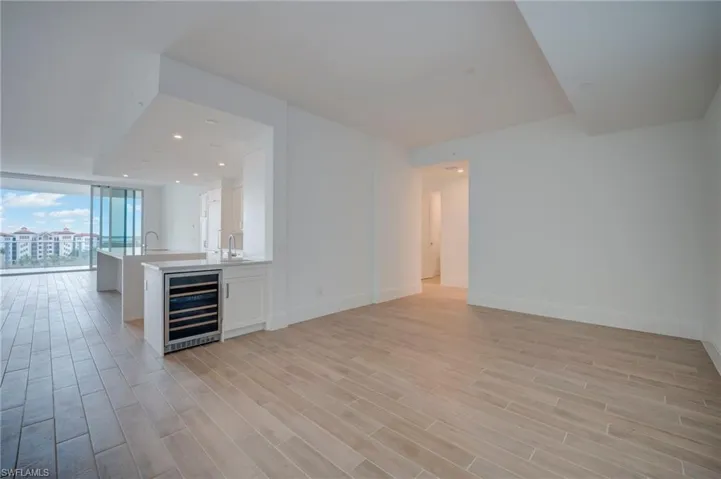 Bar with wine cooler, white cabinetry, light stone counters, expansive windows, and light wood-style floors