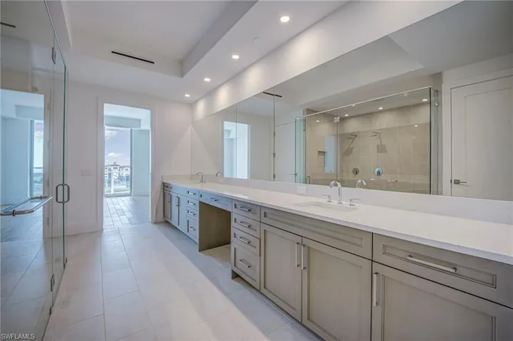 Bathroom featuring double vanity, a raised ceiling, a shower stall, recessed lighting, and light tile patterned floors