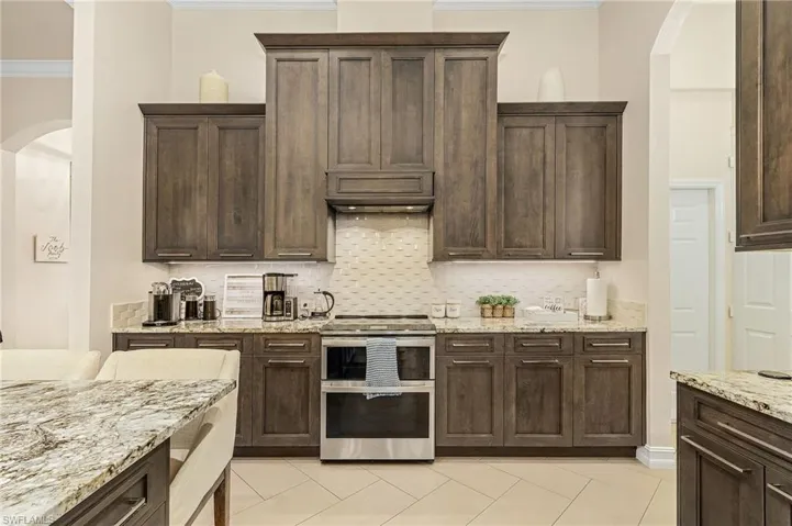 Kitchen with crown molding, light stone countertops, double oven range, tasteful backsplash, and light tile flooring