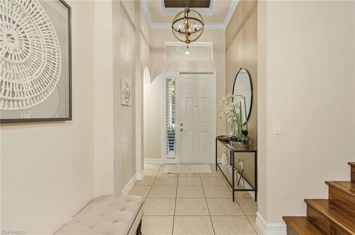 Foyer featuring an inviting chandelier, a tray ceiling, light tile floors, and crown molding