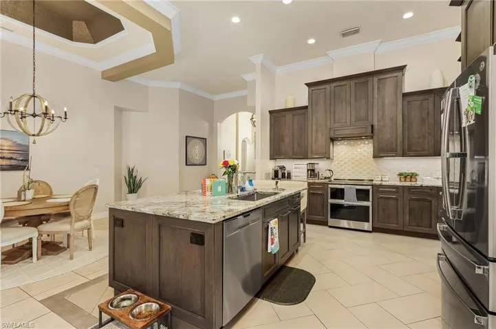 Kitchen featuring ornamental molding, stainless steel appliances, a kitchen island with sink, tasteful backsplash, and light tile floors