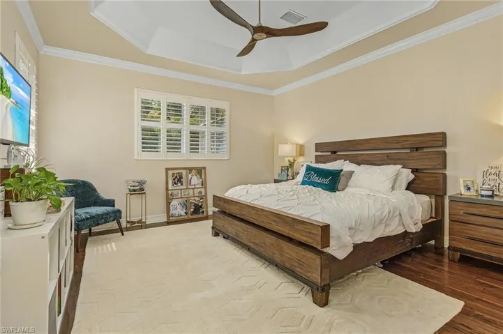 Bedroom with ornamental molding, hardwood / wood-style floors, ceiling fan, and a raised ceiling