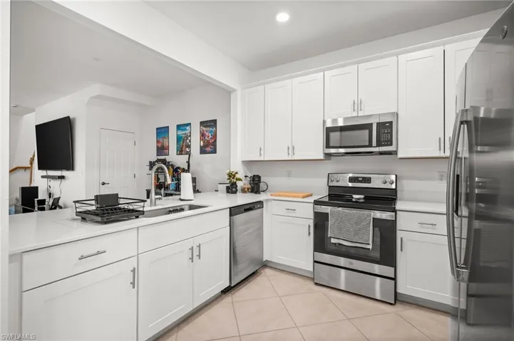 Kitchen with appliances with stainless steel finishes, white cabinets, light tile patterned flooring, recessed lighting, and a peninsula