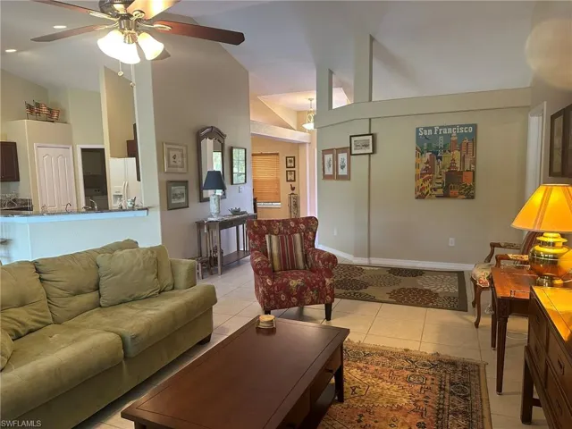 Living area featuring high vaulted ceiling, ceiling fan, baseboards, and light tile patterned floors