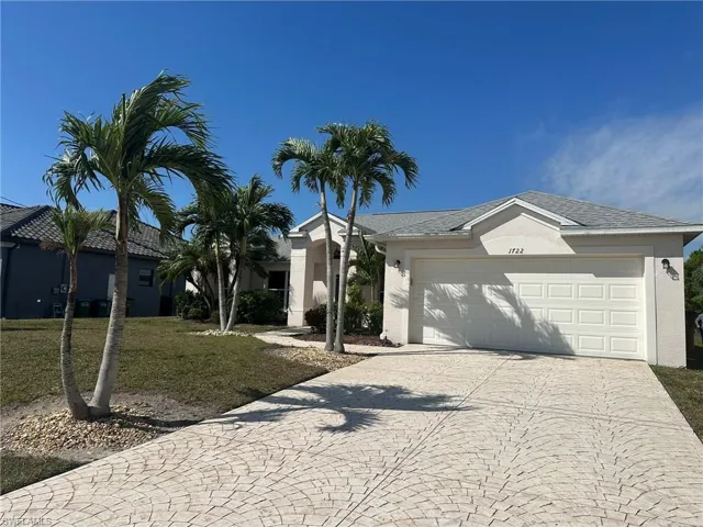 Ranch-style home featuring an attached garage, a front lawn, decorative driveway, and stucco siding