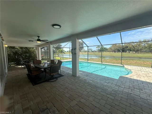 Outdoor pool with outdoor dining space, a patio, ceiling fan, a water view, and glass enclosure