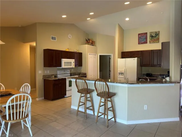 Kitchen with visible vents, high vaulted ceiling, white appliances, and dark stone counters