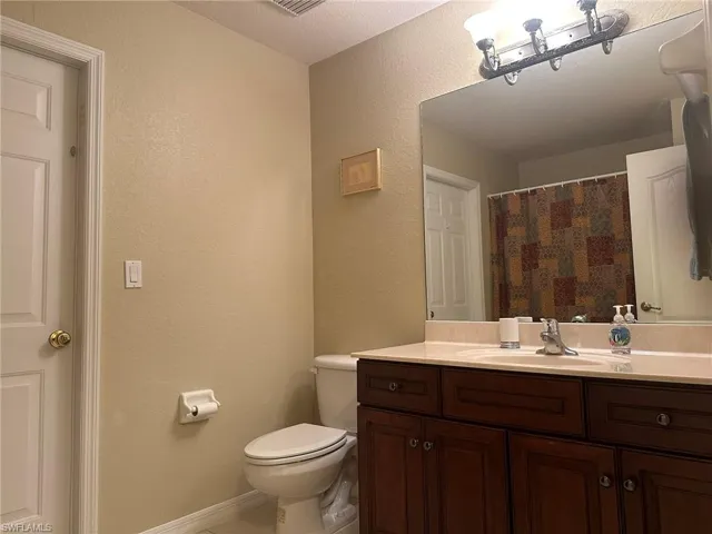 Bathroom with a textured wall, toilet, vanity, and baseboards
