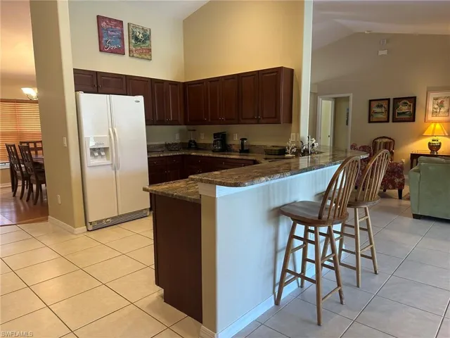 Kitchen featuring dark stone countertops, light tile patterned floors, a sink, a peninsula, and white refrigerator with ice dispenser