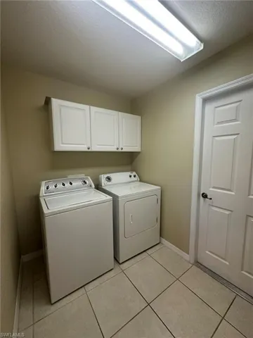 Laundry area featuring washer and dryer, light tile patterned flooring, baseboards, and cabinet space