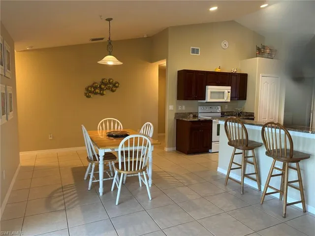 Dining space featuring light tile patterned flooring, high vaulted ceiling, baseboards, and visible vents