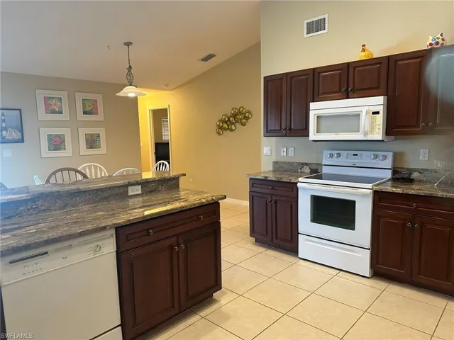 Kitchen with light tile patterned flooring, lofted ceiling, white appliances, and visible vents