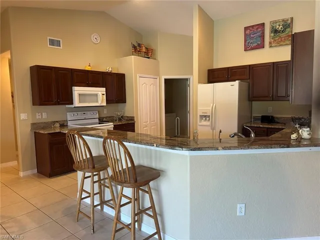 Kitchen featuring white appliances, a peninsula, visible vents, dark stone counters, and high vaulted ceiling