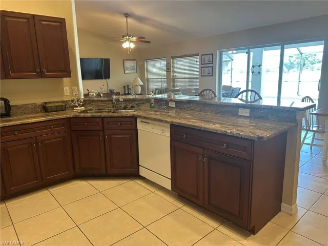Kitchen featuring white dishwasher, a sink, light tile patterned floors, and a healthy amount of sunlight