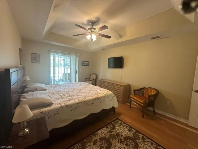 Bedroom featuring access to outside, light wood-type flooring, a ceiling fan, visible vents, and a raised ceiling