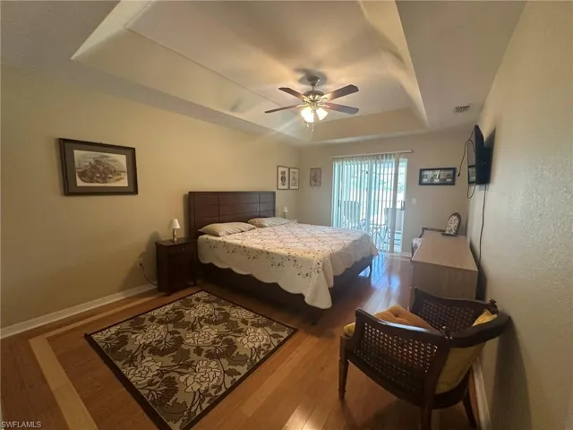 Bedroom with a ceiling fan, visible vents, access to exterior, a raised ceiling, and wood finished floors