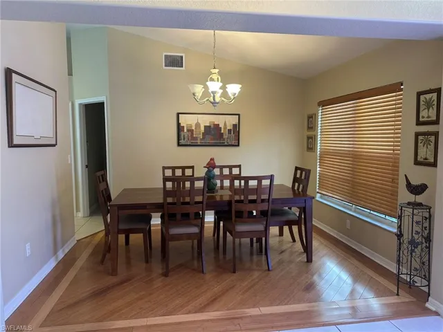 Dining space with light wood-style flooring, visible vents, a chandelier, lofted ceiling, and baseboards