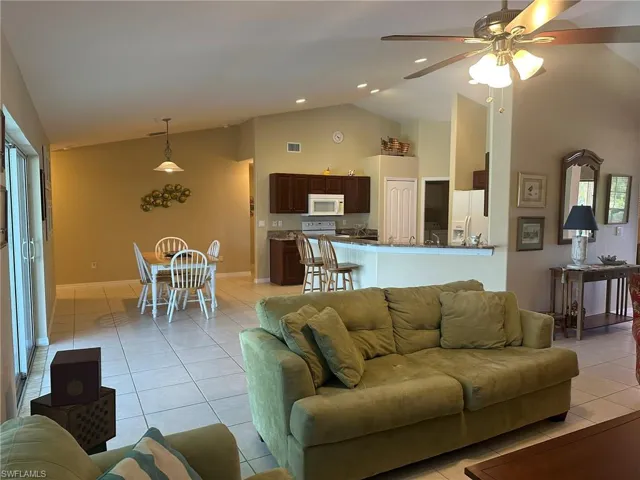 Living room with high vaulted ceiling, light tile patterned floors, ceiling fan, visible vents, and baseboards