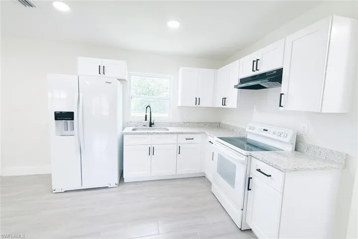 Kitchen with white appliances, white cabinets, under cabinet range hood, and recessed lighting