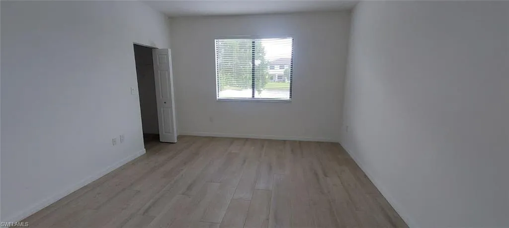 Light-toned wood-finish flooring, white painted walls, and a window with blinds