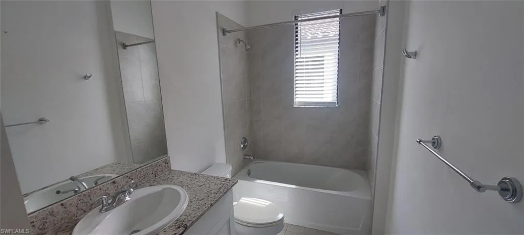 Bathroom featuring a white bathtub, tiled shower surround, window with blinds, vanity with a white oval sink, and a speckled countertop